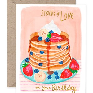 Puede incluir: Tarjeta de felicitación de cumpleaños con una ilustración de acuarela de una pila de panqueques cubiertos con crema batida, arándanos, fresas y rodajas de plátano. El texto "Stacks of Love" y "on your Birthday" está en oro.