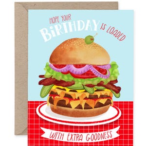 May include: A birthday greeting card featuring a watercolor illustration of a loaded burger. The card reads "Hope Your Birthday is Loaded With Extra Goodness." The burger includes a bun, lettuce, tomato, onion, pickles, and cheese.