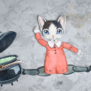 May include: A paper doll of a cat wearing a red dress and a white collar, holding a black cauldron with green liquid and a wooden spoon. The cat is wearing black tights and black shoes. A black witch's hat is on the ground next to the cat.