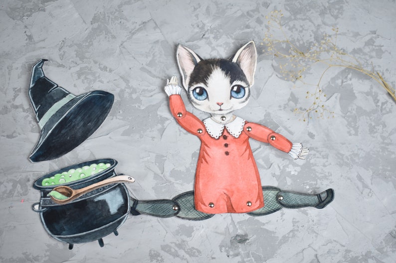 May include: A paper doll of a cat wearing a red dress and a white collar, holding a black cauldron with green liquid and a wooden spoon. The cat is wearing black tights and black shoes. A black witch's hat is on the ground next to the cat.