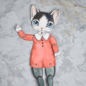 May include: A paper doll of a cat wearing a red dress with a white collar and black tights. The doll has blue eyes and black and white fur. The doll is posed with one arm raised and is on a grey background.