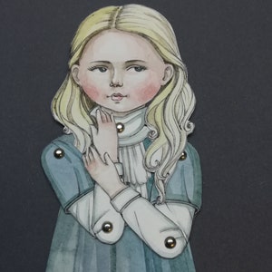 May include: A watercolor illustration of a young girl with long, wavy blonde hair and rosy cheeks. She wears a blue dress with white sleeves and a white collar. The figure is articulated with metal brads, suggesting a paper doll or similar craft.