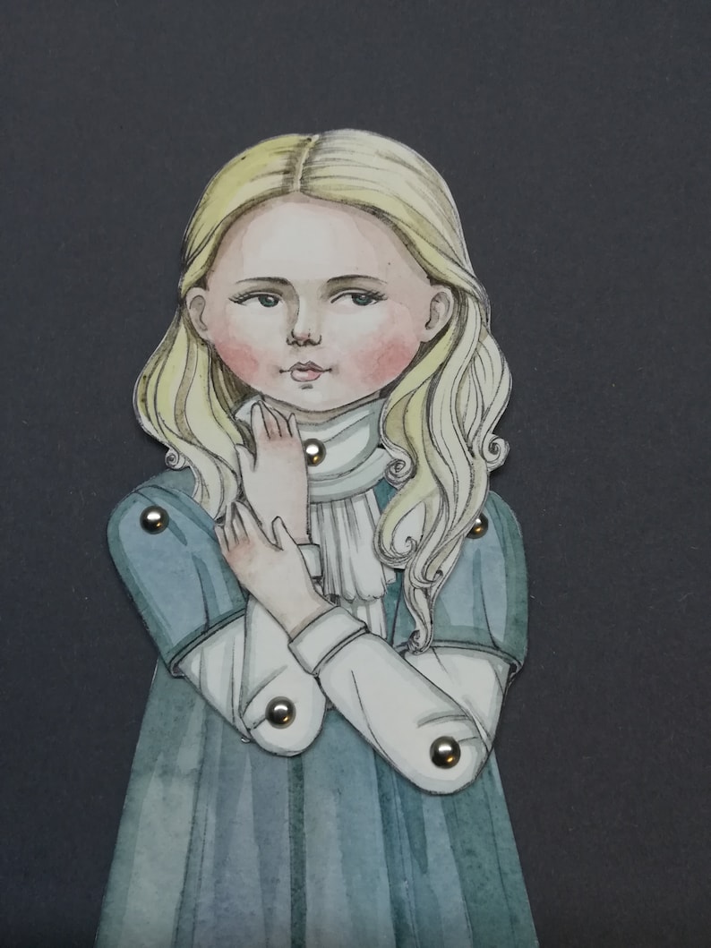 May include: A watercolor illustration of a young girl with long, wavy blonde hair and rosy cheeks. She wears a blue dress with white sleeves and a white collar. The figure is articulated with metal brads, suggesting a paper doll or similar craft.