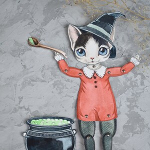 May include: A black and white cat wearing a witch's hat and red dress holds a wooden spoon over a cauldron filled with green liquid. The cat is a paper doll with movable arms and legs.