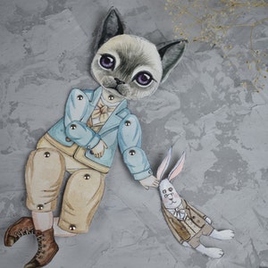 Puede incluir: Una mu&ntilde;eca de papel caprichosa con un gato con una chaqueta azul claro y pantalones color beige, tomados de la mano de un conejo con un traje marr&oacute;n. El gato tiene ojos morados y botas marrones. La mu&ntilde;eca est&aacute; sobre un fondo gris texturizado.