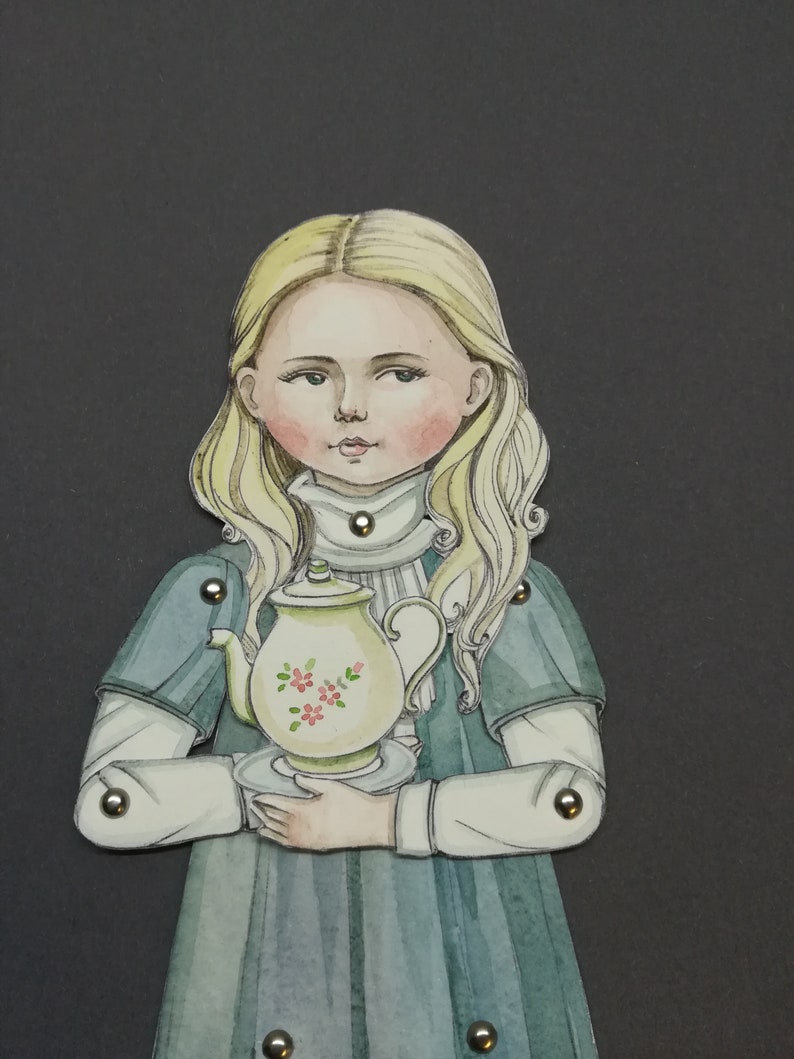 May include: A paper doll illustration of a girl with blonde hair, wearing a blue dress and holding a teapot. The teapot is cream-colored with pink floral accents. The doll has articulated joints with metal fasteners.