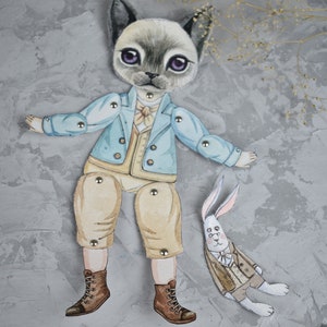 Puede incluir: Una mu&ntilde;eca de papel caprichosa con un personaje de gato con una chaqueta azul claro, pantalones color canela y botas marrones. Tambi&eacute;n hay una mu&ntilde;eca de conejo a juego. Las mu&ntilde;ecas est&aacute;n conectadas con sujetadores met&aacute;licos. Fondo gris texturizado.