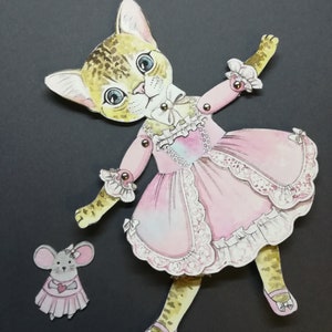 May include: A paper doll of a cat wearing a pink dress with lace trim and a white bow. The cat has brown and black spots and blue eyes. A smaller paper doll of a mouse wearing a pink dress with a heart is also included.