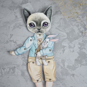 Puede incluir: Una mu&ntilde;eca de papel articulada con forma de gato, vestida con una chaqueta azul claro, pantalones cortos beige y botas marrones. La mu&ntilde;eca gato sostiene una mu&ntilde;eca de conejo blanco. Fondo gris texturizado.