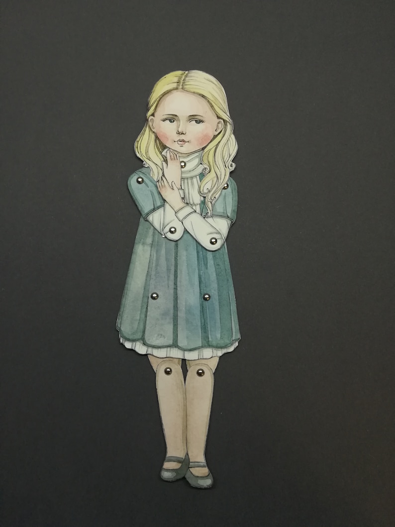 May include: A watercolor illustration of a paper doll with blonde hair and a teal dress. The doll has articulated joints and is posed with hands near the face. The background is a solid dark gray.