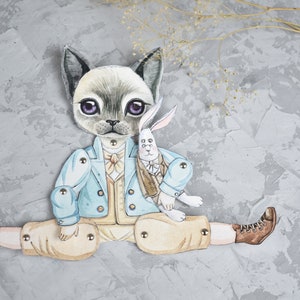 Puede incluir: Una mu&ntilde;eca de papel articulada y caprichosa con un personaje de gato con una chaqueta azul claro y pantalones color canela, sosteniendo una mu&ntilde;eca de conejo. El gato tiene ojos morados y lleva una pajarita. El fondo es gris texturizado.