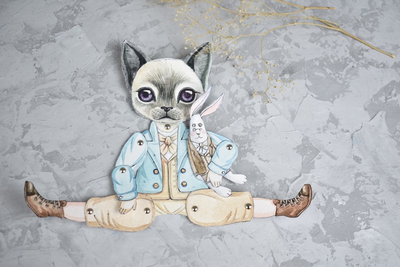 Puede incluir: Una mu&ntilde;eca de papel articulada y caprichosa con un personaje de gato con una chaqueta azul claro y pantalones color canela, sosteniendo una mu&ntilde;eca de conejo. El gato tiene ojos morados y lleva una pajarita. El fondo es gris texturizado.
