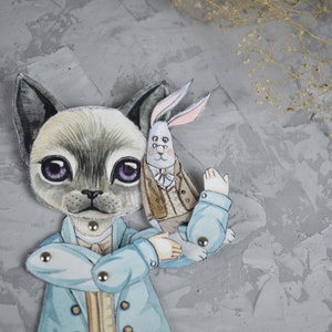 Puede incluir: Un recorte de papel caprichoso con un personaje felino con un abrigo azul claro, sosteniendo una figura de conejo. El gato tiene pelaje gris, ojos morados grandes y est&aacute; adornado con sujetadores met&aacute;licos. El conejo lleva un abrigo marr&oacute;n.