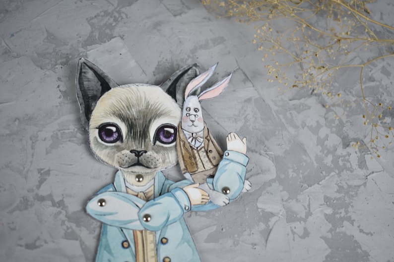 Puede incluir: Un recorte de papel caprichoso con un personaje felino con un abrigo azul claro, sosteniendo una figura de conejo. El gato tiene pelaje gris, ojos morados grandes y est&aacute; adornado con sujetadores met&aacute;licos. El conejo lleva un abrigo marr&oacute;n.