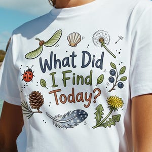 Può includere: Una t-shirt bianca a maniche corte con una stampa grafica colorata con il testo "What Did I Find Today?" circondato da illustrazioni di una coccinella, una pigna, una piuma, un dente di leone, bacche, una conchiglia e un seme alato.