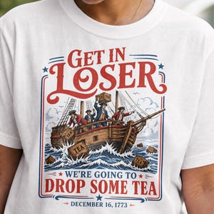 Puede incluir: Camiseta blanca con un diseño que representa un barco de la época colonial y el texto "GET IN LOSER, WE'RE GOING TO DROP SOME TEA, DECEMBER 16, 1773." El diseño incluye colores rojo, azul y marrón.