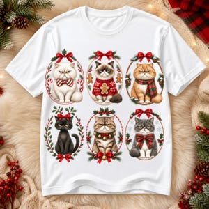 May include: A white short-sleeved t-shirt featuring a graphic print of six grumpy cats arranged in two rows. Each cat is framed by a holiday-themed wreath with red bows, showcasing various festive accessories like plaid scarves, bows, and sweaters.