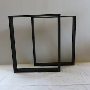 May include: Two black metal table legs with a rectangular frame. The legs are made of sturdy metal and have a simple, modern design.