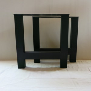 May include: Two black, welded steel table legs. Each leg has a rectangular frame with a square base and top. The legs are designed for a modern, industrial aesthetic and are suitable for various table sizes.