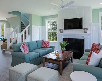Könnte beinhalten: Ein Wohnzimmer mit zwei blauen Sofas, einem Couchtisch und einem Kamin. Die Sofas haben rote und weiße Kissen. Der Raum hat große Fenster mit Blick auf Bäume.