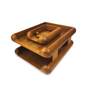 May include: A two-tiered wooden desk organiser featuring a rectangular base tray and a smaller, matching rectangular tray stacked on top. Both trays are crafted from medium-toned wood with rounded edges and a smooth finish, designed for document storage.
