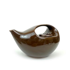 May include: A glossy, brown ceramic teapot with a unique, rounded shape and a large handle. The spout is slender, and the lid is small and circular. The teapot is designed for pouring and serving tea.