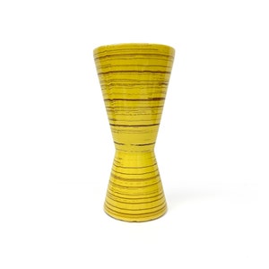 May include: A yellow ceramic vase with brown stripes. The vase has a wide mouth and a narrow base.