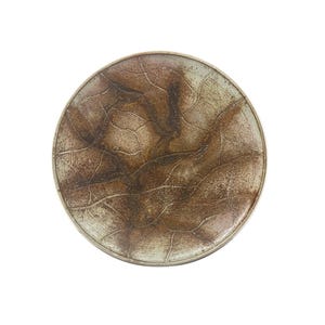 May include: A round ceramic plate with a white glaze and brown and pink accents. The plate has a textured surface with a pattern of lines and swirls.