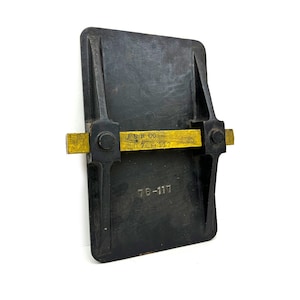 May include: A black metal plate with a brass ruler attached to it. The ruler has the text "A.S.B. CO. 76-117" on it. The plate also has the number "76-117" printed on it.