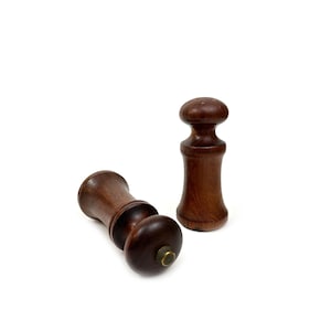 May include: Two wooden salt and pepper shakers with a dark brown finish. The shakers have a round top and a cylindrical body.
