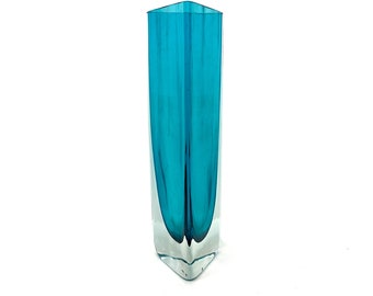 Könnte beinhalten: Eine türkisblaue Glasvase mit einem klaren Glasfuß. Die Vase hat eine rechteckige Form mit einer leicht ausgestellten Öffnung.