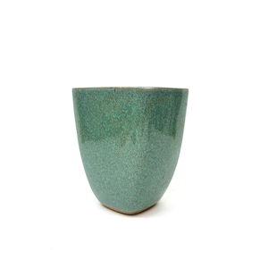 May include: A handcrafted, teal-colored ceramic cup with a speckled glaze. The cup has a rounded, tapered shape and a slightly flared rim. The exterior has a textured appearance, and the bottom is flat. The cup is suitable for beverages.
