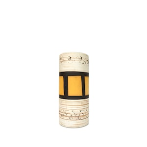 May include: A white ceramic vase with a brown and yellow geometric pattern. The vase has a cylindrical shape and a textured surface.