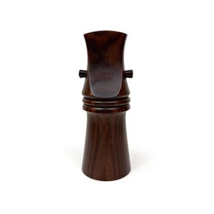 Może przedstawiać: Drewniana rzeźba w ciemnym kolorze brązu o unikalnym wzorze. Rzeźba ma zaokrągloną podstawę i wysoki, smukły szyję z zakrzywionym wierzchołkiem.