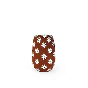 May include: A brown, cylindrical decorative object with white flower patterns. The object has a rounded top and bottom, and the white flower shapes are evenly spaced across the surface.
