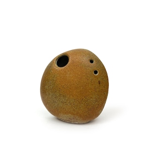 May include: A brown, egg-shaped ceramic ocarina with three small holes and one large hole. The ocarina has a speckled texture and is set against a white background. This musical instrument is a wind instrument.