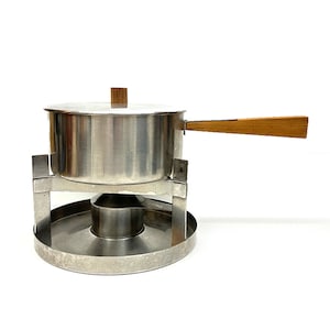 Könnte beinhalten: Ein silberner Fonduetopf mit einem Holzgriff und einem Deckel. Der Topf steht auf einem Metallständer mit einem runden Sockel.