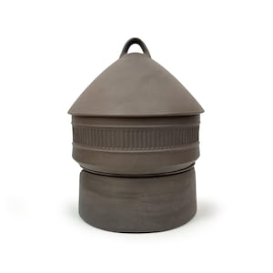 Puede incluir: Un recipiente de cerámica marrón con tapa y asa. El recipiente tiene una banda decorativa alrededor del medio.