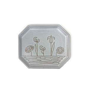 May include: A light gray octagonal ceramic dish with a hand-drawn design of five flowers in brown. The flowers are a tulip, two daisies, and two other flowers.