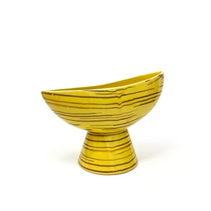 Può includere: Un vaso in ceramica giallo con strisce marroni. Il vaso ha una ciotola larga e arrotondata e una base cilindrica stretta.