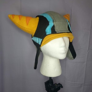 May include: A black, gray, and blue fleece hat with yellow horns. The hat has ear flaps and is worn on a white mannequin head.