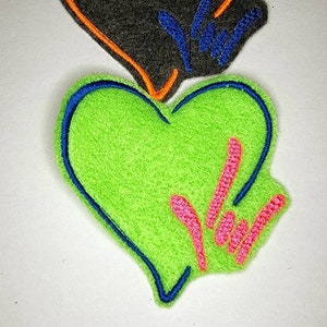May include: Two heart-shaped patches. The top patch is black with an orange outline and blue hand gesture. The bottom patch is bright green with a blue outline and pink hand gesture. Both patches are on a white background.
