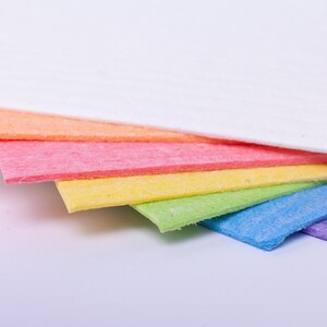 May include: A stack of colorful cleaning cloths in a rainbow of hues. The cloths are arranged in a fan shape, showcasing the white, orange, pink, yellow, green, blue, and purple colors. The cloths are made of a textured material.