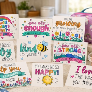 Könnte beinhalten: Eine Sammlung farbenfroher, illustrierter Karten mit positiven Affirmationen. Jede Karte zeigt handgeschriebene Sätze wie „Du bist genug“, „Du bringst Freude“ und „Ich liebe die Art, wie du denkst“. Ein Lunchpaket mit Einhörnern und ein grüner Apfel sind ebenfalls im Bild.