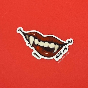 May include: A sticker featuring a stylized illustration of a mouth with red lips and sharp fangs. The words "Bite Me" are written in black script. The sticker is on a red background.