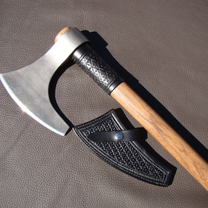 May include: A silver axe with a wooden handle and a black leather sheath. The axe has a curved blade and a decorative handle.