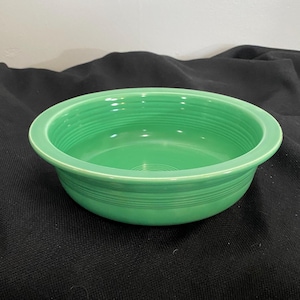 May include: A green ceramic bowl with a wide rim and a smooth, glossy finish. The bowl has a simple, classic design with subtle ridges around the rim.