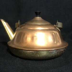 May include: A vintage copper and brass teapot with a black knob on the lid. The teapot has a rounded body and a spout with a flared opening.