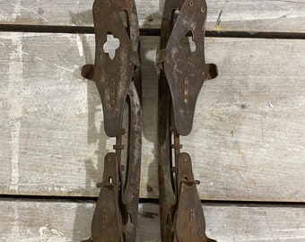 May include: A pair of antique rusty metal ice skates with a clover-shaped design and the text "WILSON'S 10 1/2" on the right skate.
