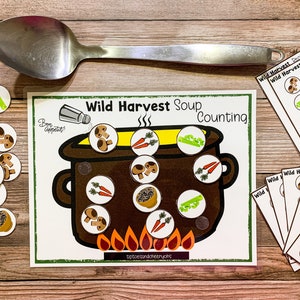 May include: A printable game for kids featuring a brown pot with yellow soup and various ingredients like mushrooms, carrots, and celery. The game includes counting cards with numbers 1, 2, and 5. The text on the game board reads "Wild Harvest Soup Counting".